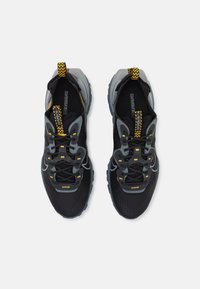 Černé sportovní boty s šedými detaily, texturovaným s íťovaným svrškem, žlutými tkaničkami a robustním vzorkem podešve. Lehká a prodyšná konstrukce.