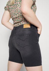 Black denim shorts with a fitted design, featuring rear pockets and a leather label on the waistband. Floral print top partially visible.
