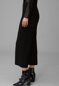 Svarta virkade culotter med hög midja, kompletterade med glänsande svarta ankelstövlar med spetsig tå och kraftig klack.