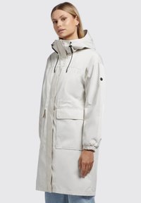 Parka bianca impermeabile con cappuccio, polsini elasticizzati, tasche frontali e chiusura con cerniera. Presenta accenti neri a contrasto. Texture liscia.