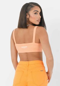 Perzikkleurige geribbelde crop top met brede schouderbanden en logo detail op de rug, gecombineerd met hooggesneden oranje denim shorts.