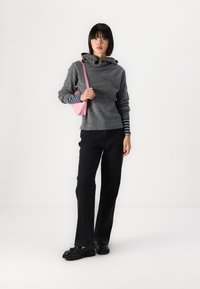 Sudadera gris con capucha y puños acanalados sobre una camiseta de rayas de manga larga, combinada con pantalones negros y zapatos negros; sosteniendo un bolso rosa.