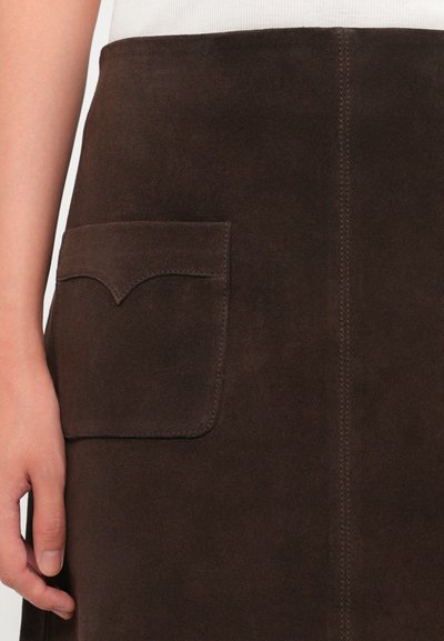 Pruunist suede'ist seelik, millel on üks tasku, millel on kõver õmblusdetail, esitledes siledaid tekstuure ja puhtaid jooni.