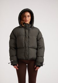 Giacca a vento imbottita verde scuro con cappuccio, design trapuntato e polsini regolabili. Materiale leggero, dotata di chiusura frontale con zip.