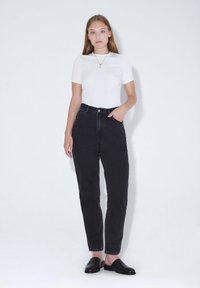 Weißes Kurzarm-T-Shirt und hoch taillierte schwarze Denim-Jeans mit einer schmalen Passform. Schwarze Slipper runden das Outfit ab.