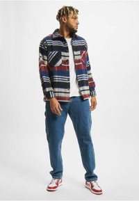 Károvaná flanelová košile v modré, červené a bílé barvě, zapínaná vpředu, spárovaná s modrými denimovými džíny a červenobílými teniskami.