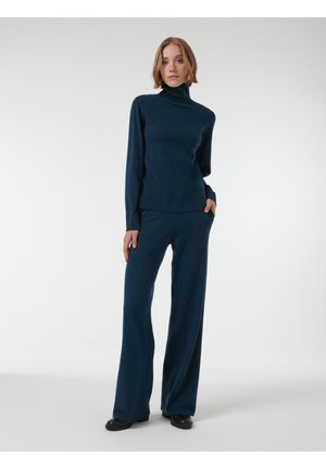 Donker teal brei turtleneck trui en bijpassende broek met wijde pijpen, gemaakt van zachte, gestructureerde stof; heeft lange mouwen en voorzakken.