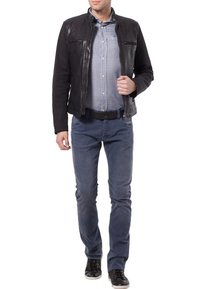 Mężczyzna w czarnej skórzanej kurtce, pod którą ma jasnoniebieską koszulę z guzikami, niebieskich dżinsach, czarnym pasku i czarnych trampkach, idzie do przodu.