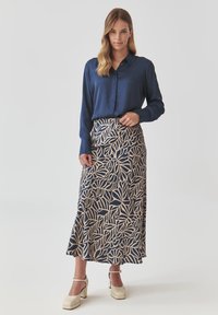 Blouse à manches longues bleu marine, associée à une jupe beige et bleu marine à motifs avec des motifs de feuilles, complétée par des talons blocs de couleur claire.