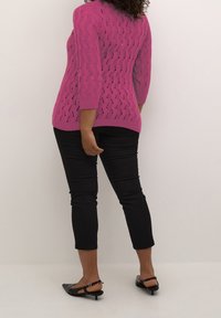 Pull en maille magenta avec un motif ondulé ouvert, manches trois-quarts et ourlet arrondi. Associé à un pantalon noir ajusté et des chaussures slingback noires.