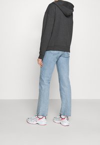 Donkergrijze hoodie, lichtblauwe rechtlopende jeans en grijs, wit en roze sneakers. Casual outfit gezien van achteren.