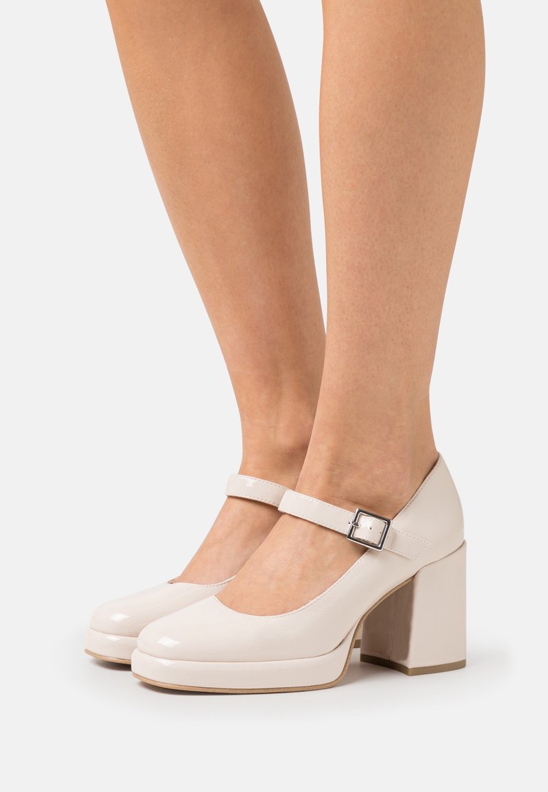 Chaussures Mary Jane en cuir verni beige avec un bout rond, un talon épais en bloc et une bride réglable avec une boucle métallique. Texture lisse.