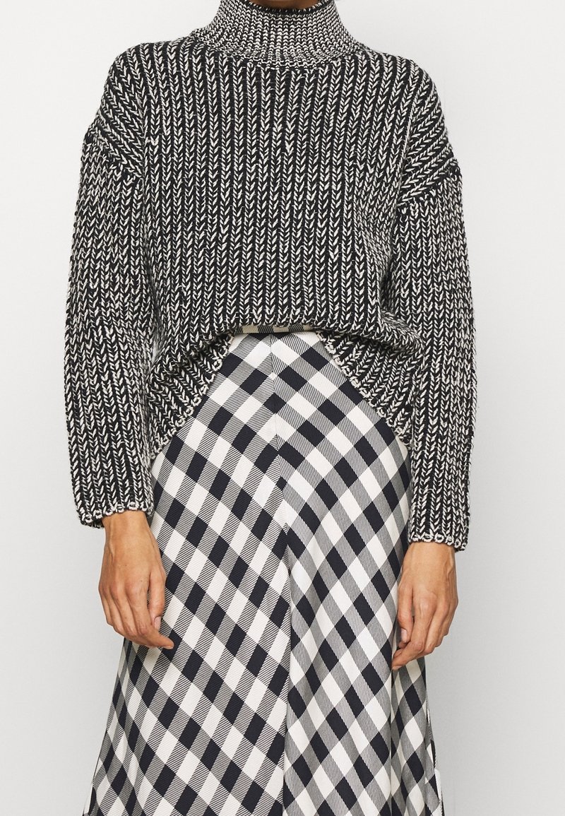 Black and white knitted sweater with a high collar and loose fit; paired with a checkered skirt in alternating black and white squares.