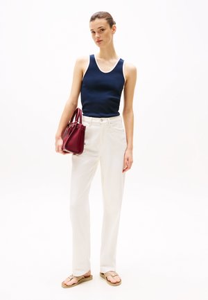 Navy tank top with white trim, white straight-leg pants, and tan flip-flops. Holding a small burgundy handbag with gold hardware accents.