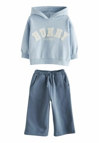 Világoskék kapucnis pulóver "BUNNY ACADEMY" hímzett bézs felirattal, és hozzá illő kék melegítőnadrág, rugalmas derékkal és oldalzsebekkel.