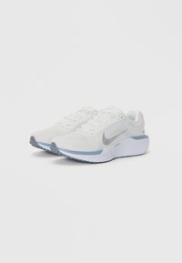 Hvit treningssko med en pustende mesh-overdel, med en grå Nike-swoosh, lyseblå detaljer og en polstret såle.