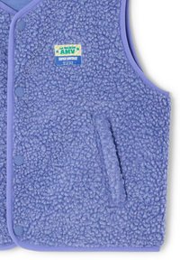 Veste en polaire violet clair avec une texture duveteuse, une bordure violette unie contrastante et une poche frontale. Présente une étiquette de marque sur la poitrine.