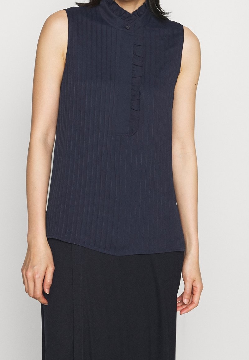 Námořnická bezramínková blůza s vertikálními pruhy, s volánkovým límcem a knoflíkovou légou. Tkanina vypadá hladce s mírným leskem.