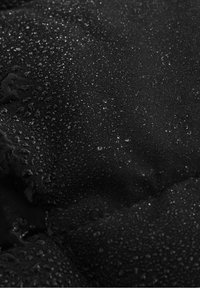 Czarny materiał o teksturowanej powierzchni, z licznymi małymi kroplami wody, co wskazuje na odporność na wilgoć lub właściwości wodoodporne.