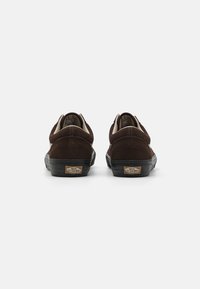 Smeđe nubuk cipele s niskim profilom, crnom gumenom petom i krem oblogom. Sadrži "Vans Off The Wall" logo na peti.