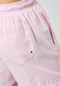 Lyserosa shorts laget av vevd stoff med rutete mønster. Har strikk i livet og en sidelomme med metallknapp.