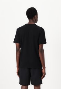 Zwarte katoenen t-shirt met korte mouwen en een ronde hals, gezien vanaf de achterkant, gecombineerd met zwarte shorts. Vlotte textuur, casual ontwerp.