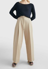 Haut bleu marine à manches longues associé à un pantalon beige taille haute à jambes larges avec un motif texturé ; sandales plateforme noires avec des accents tissés.