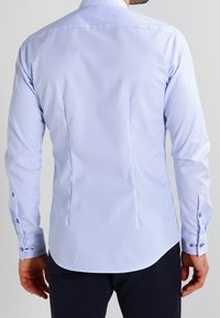 Camicetta a righe azzurro chiaro e bianco, con maniche lunghe, colletto a punta, cuciture curate e polsini con bottoni, taglio aderente e orlo curvo.