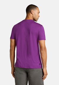 Lilla kortærmet t-shirt, rund hals, tekstureret stof, har en ligekant, båret med grå shorts, set fra ryggen.