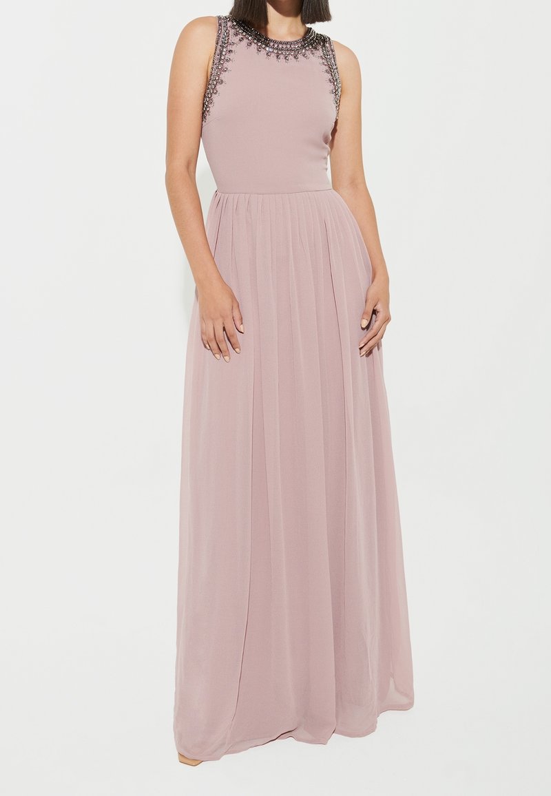 Robe longue sans manches en rose pâle, avec un col orné de perles, une jupe fluide et un tissu léger avec une texture douce.