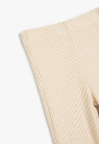 Tejido de punto beige con un patrón texturizado, que presenta un diseño ajustado y una cinturilla elástica para mayor comodidad y flexibilidad.