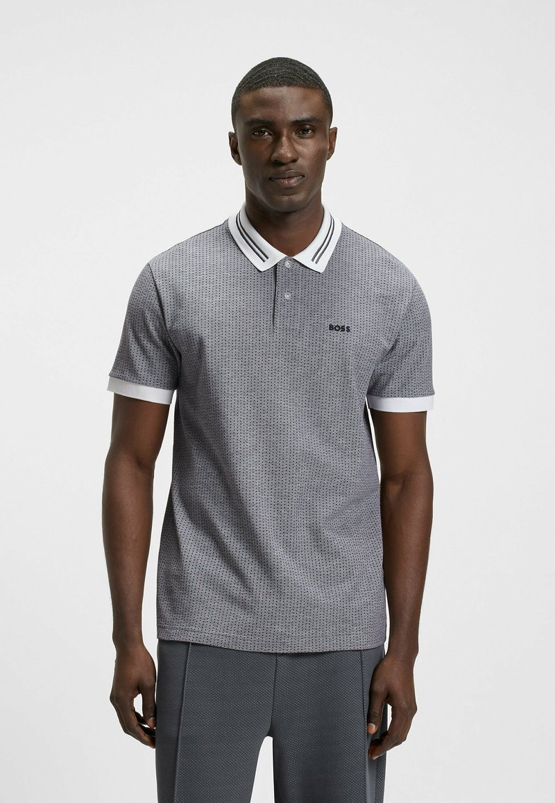 Harmaa kuviollinen polo-paita, jossa on kaksipainikeoikeus, valkoinen kaulus ja hihansuut, joissa on mustat raidat, sekä pieni logo rinnassa.