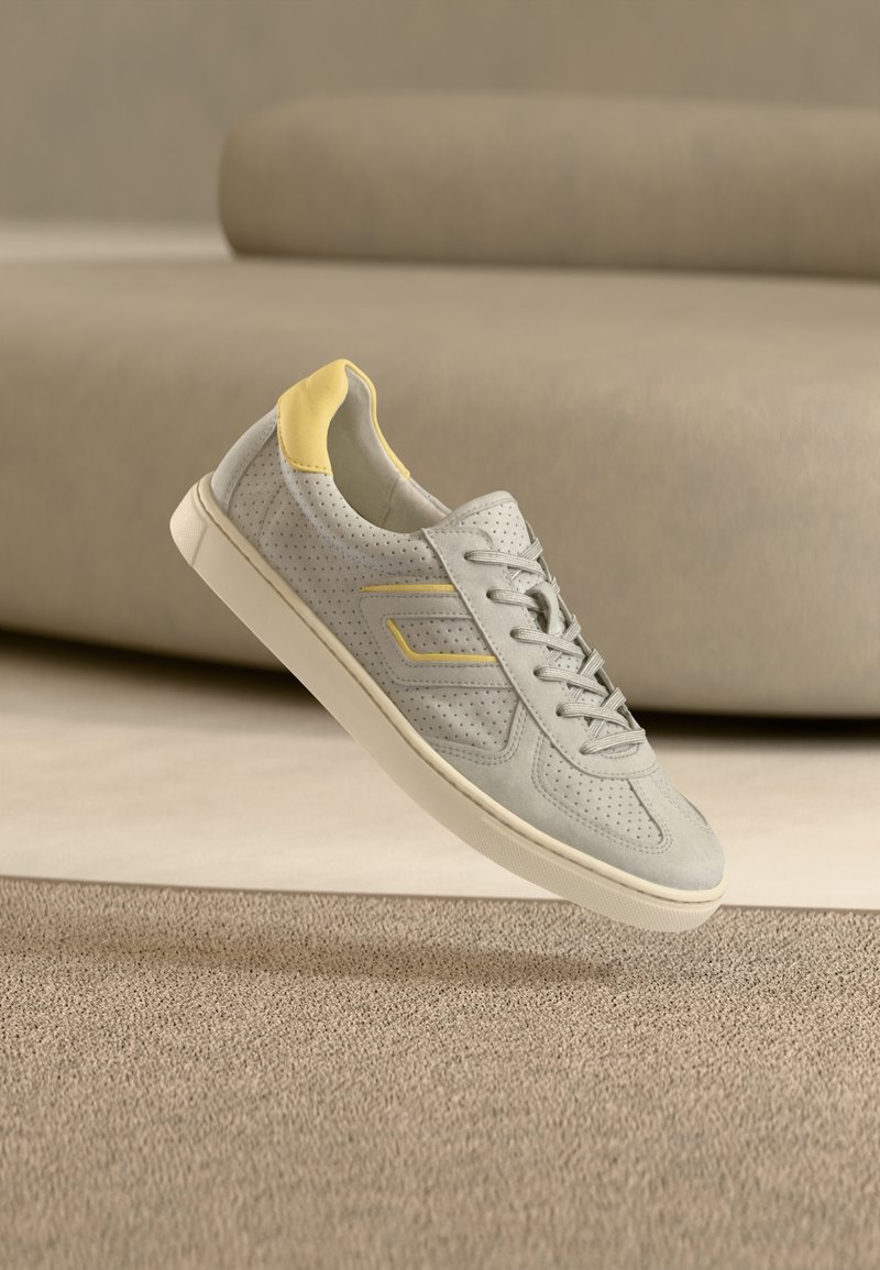 Helehall halli perforatsioonidega seemisnahast tennised, mis on kandmisel kollase aktsendiga, tasaste nööride ja valge kummist tallaga.