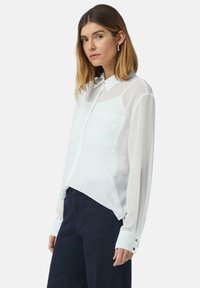 Witte sheer blouse met een kraag, lange mouwen, twee borstzakken en met knopen afsluitbare manchetten. Gladde textuur met een vloeiende uitstraling.