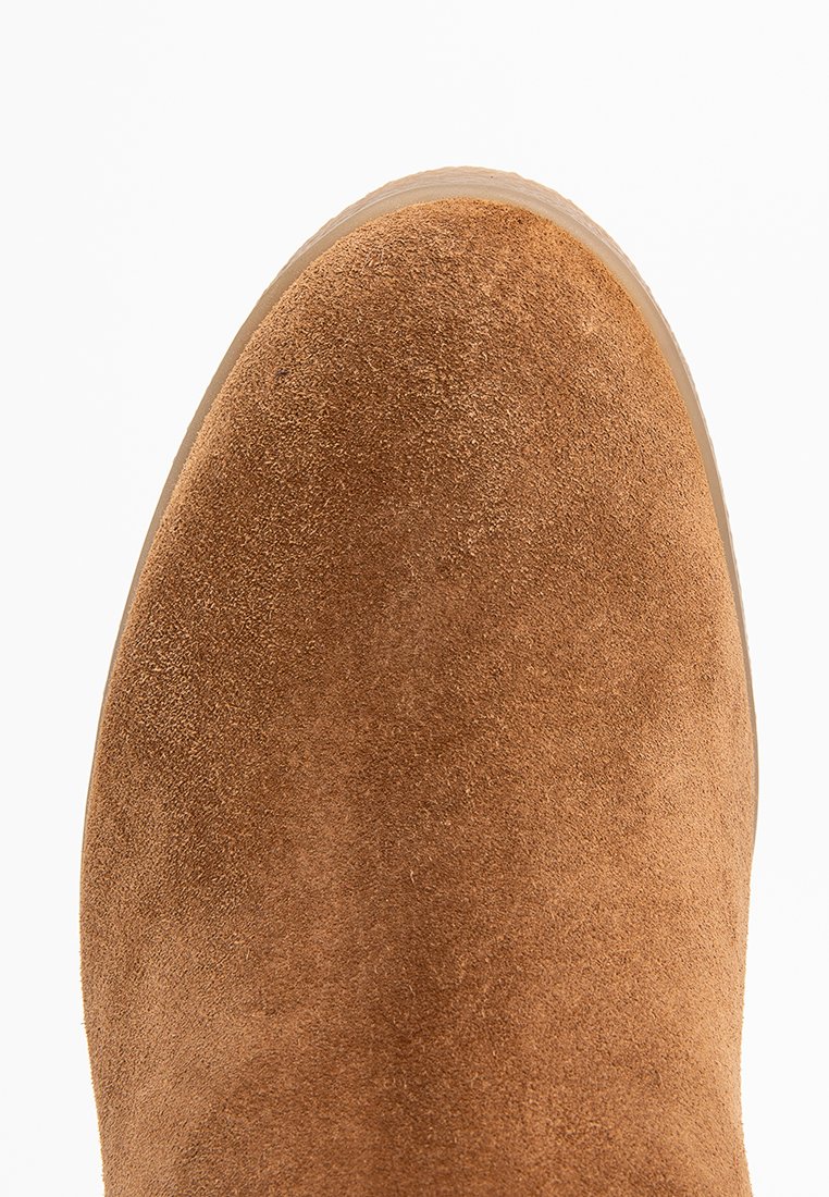 Bottine en daim marron clair avec un bout arrondi et une texture lisse. La couture latérale et la semelle en caoutchouc sont visibles, mettant en avant le design épuré.