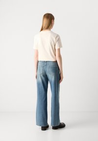 Ανοιχτό κρεμ κοντομάνικο μπλουζάκι σε συνδυασμό με ψηλοκάβαλο, ξεθωριασμένο μπλε φαρδύ τζιν, που διαθέτει δύο πίσω τσέπες και υφή στην επιφάνεια.