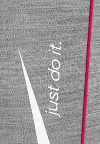 Le tissu gris présente un grand logo Swoosh blanc de Nike et le texte "just do it." Une fine touche de rouge court verticalement le long du bord. Texture douce.