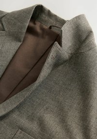 Grau kariertes Blazer mit brauner Innenausstattung, teilweise geöffnet präsentiert, wobei der strukturierte Stoff und die maßgeschneiderten Designdetails zur Geltung kommen.