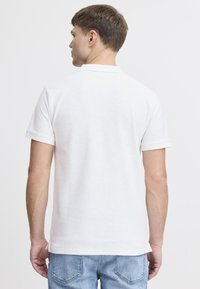 Hvit polo skjorte med korte ermer, ribbestrikket krage, teksturert stoff og sidespalter, parret med lyseblå denim jeans.