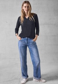 Schwarzes Langarmshirt mit V-Ausschnitt, kombiniert mit hellblauen weit geschnittenen Jeans und weißen Schuhen. Schlichtes Design mit lockerer Passform.
