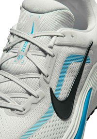 Hvid sportssko med lyseblå accenter, sort Nike swoosh og "QUEST 07" mærkat på den polstrede tunge, med hvidt mesh og snørebånd.