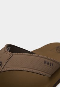 Σανδάλι της μάρκας Brown Reef με υφασμένη λωρίδα και ραμμένα άκρα σε μπεζ σόλα πάνω σε απλό φωτεινό φόντο.