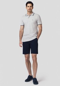 Szary polo z granatowym kołnierzykiem i wykończeniami, w połączeniu z granatowymi szortami. Model ma również na sobie ciemne buty sportowe, stoi na jasnym tle.