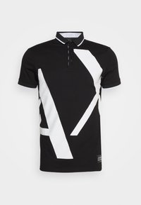 Svart pikétröja med ett stort vitt geometriskt mönster, kontrasterande krage och tre-knappslå. Tillverkad av bomull med en slät textur.