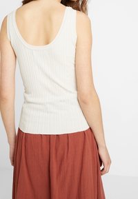 Débardeur crème côtelé avec un dos en scoop, associé à une jupe fluide couleur rouille. Accent sur la texture et la coupe ajustée du débardeur.