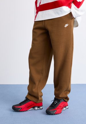 Brune Nike sweats med løs pasform, prydet med et broderet hvidt logo. Sammen med røde og sorte Nike sneakers, hvor den strukturerede sål er synlig.