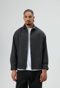 Donkergrijs overhemd met knopen, gemaakt van een gestructureerde stof met een kraag, gedragen over een wit T-shirt en gecombineerd met zwarte broek.