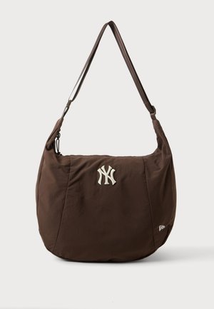 Brązowa torba na ramię z regulowanym paskiem i białym haftowanym logo New York Yankees na środku z przodu.
