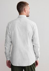 Long-sleeve shirt in light gray fabric with a subtle check pattern, featuring a standard collar and buttoned cuffs. Back view shown.
