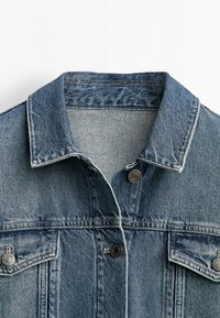 Farkkutakki, jossa on klassinen kaulus, edessä napit ja kaksi rintataskua. Vaaleansininen väri, jossa on teksturoitu farkkukangas.